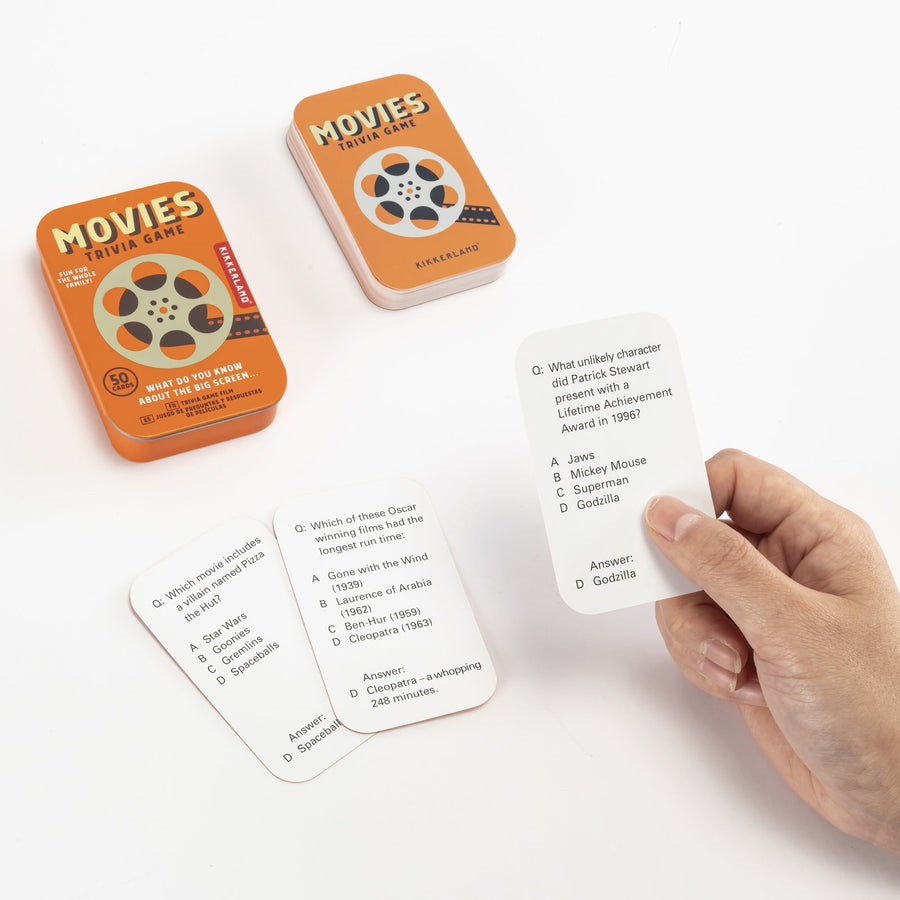 hand holding a movie trivia card with the tin and other cards arranged on a white background.