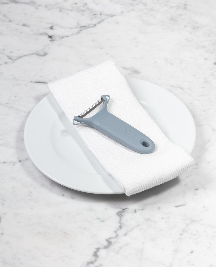 the y serrated peeler displayed on a white towel placed on a white plate sitting on a white marble countertop