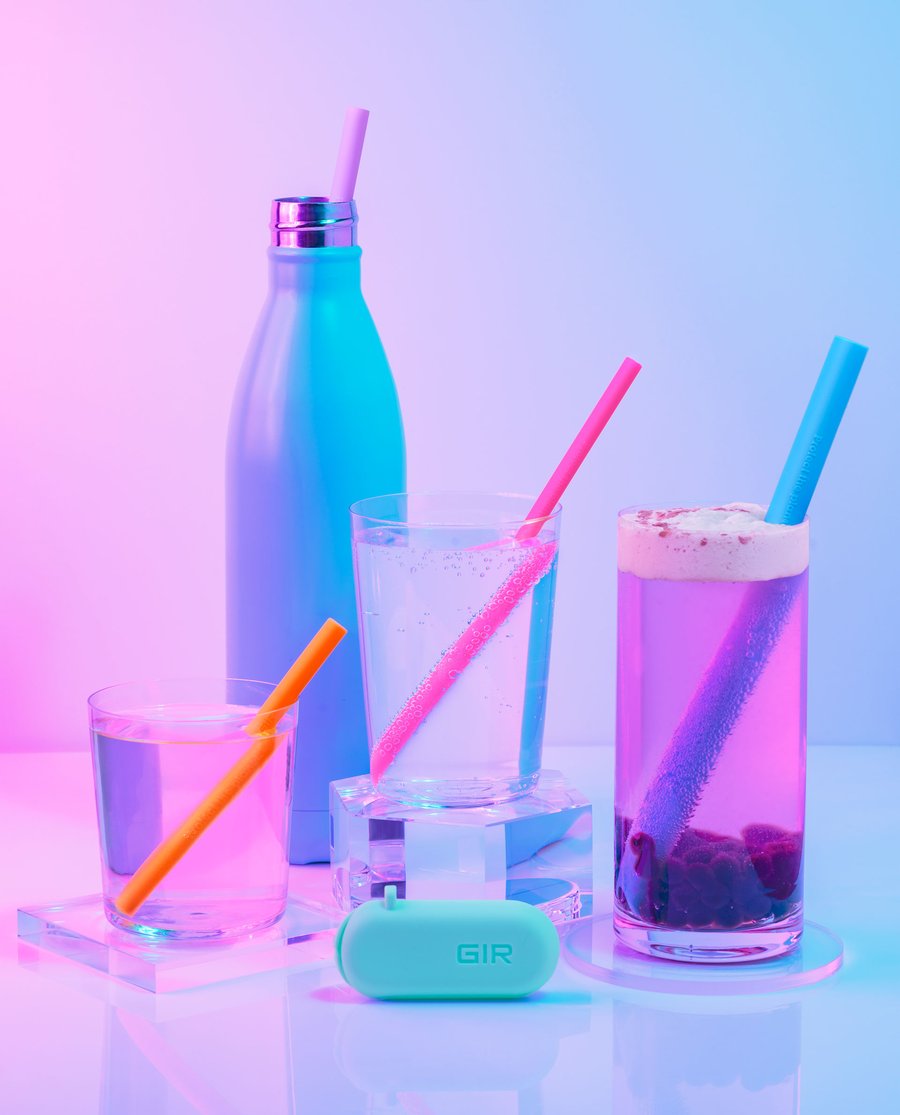 all four silicone straws displayed in different sized glasses and one in a water bottle with the travel case in front under florescent lights 