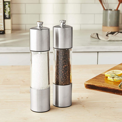 stainless steel and acrylic salt and pepper grinders on wooden kitchen counter with various kitchen tools in background