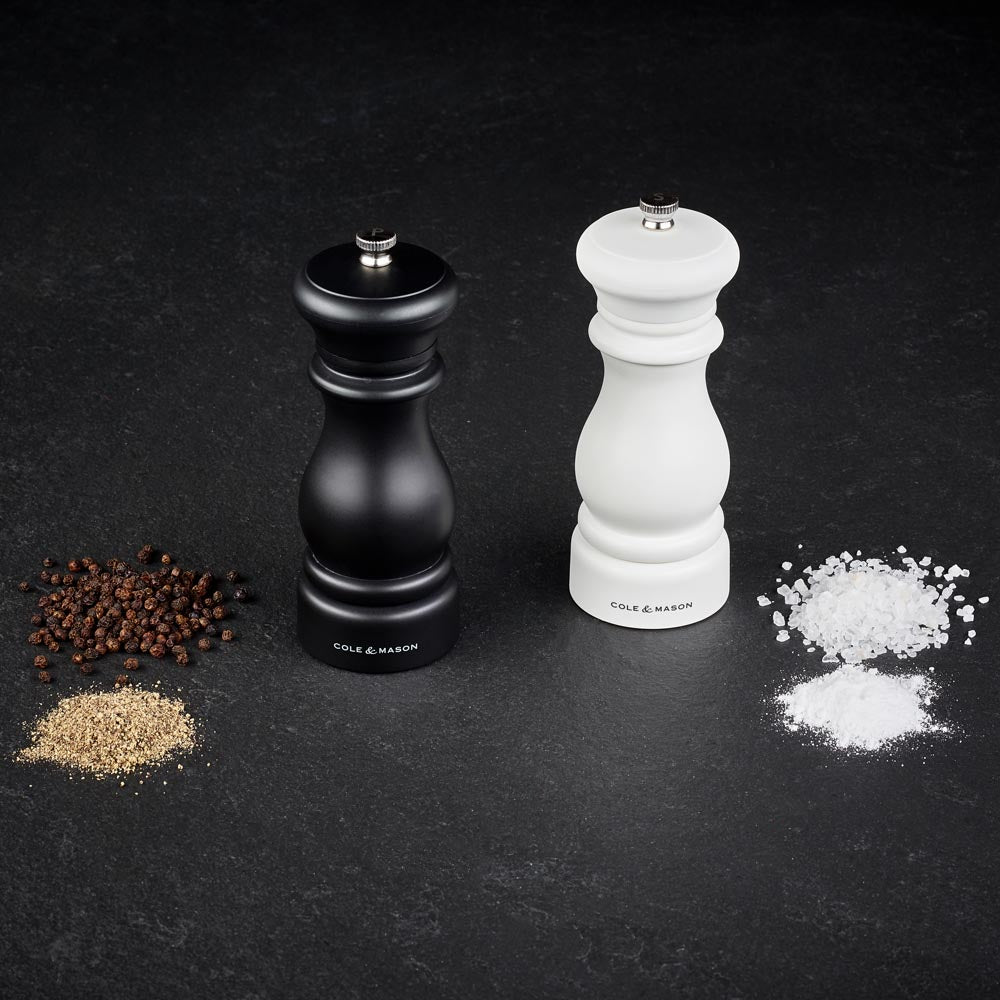 pepper grinder with whole pepper and ground pepper on left, salt grinder with salt rocks and ground salt on right, shown on black marble background