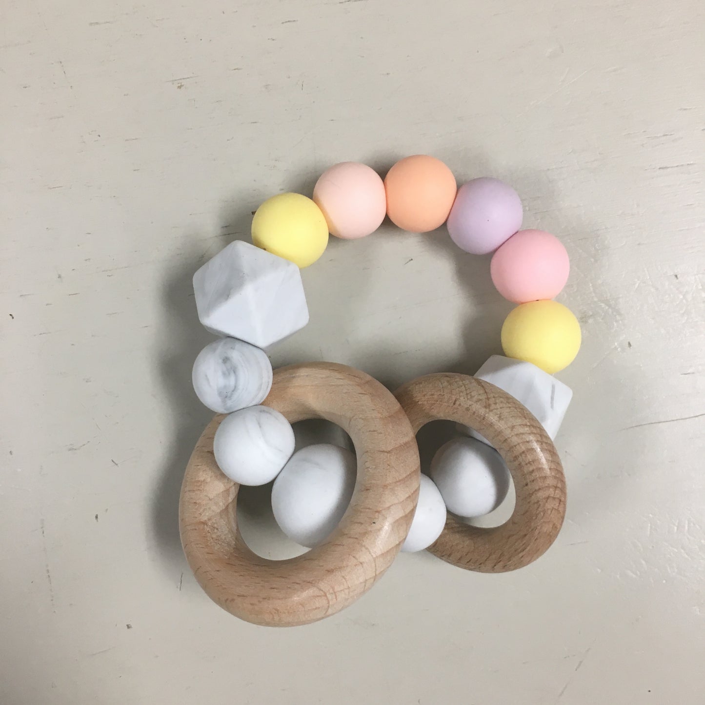 ring of silicone beads in shades of yellow, pink, and orange with two wooden rings on it.
