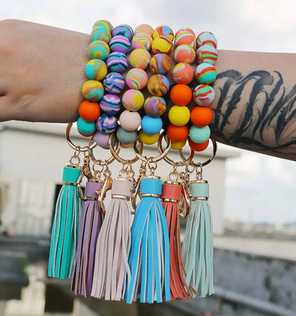 person's arm wearing 6 different colors of silicone beaded bracelets and tassels and key rings.