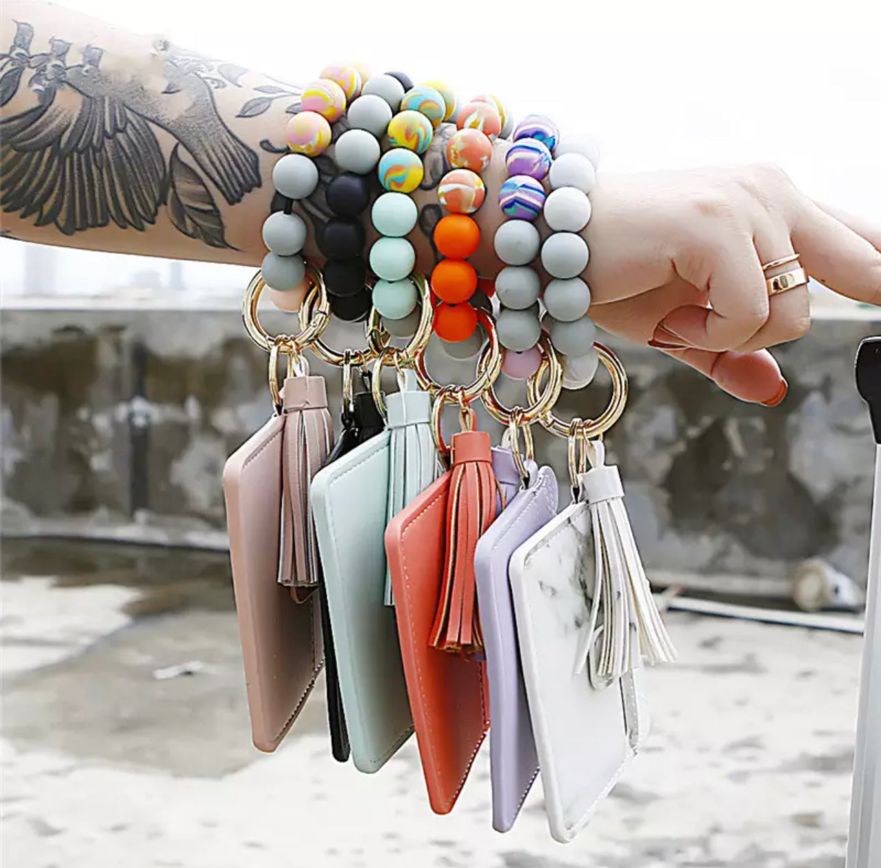 person's arm wearing 6 colorful silicone beaded bracelets with a wallet and tassel attached to them.