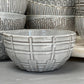 lines patterned stoneware bowls displayed in front of multiple patterned stoneware bowls on a white surface