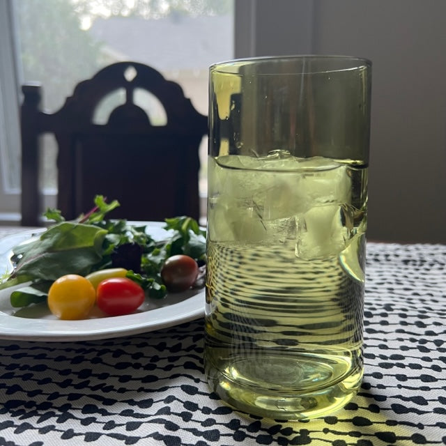 olive mid century cooler glass filled and displayed on a black and white table cloth next to a plate of salad