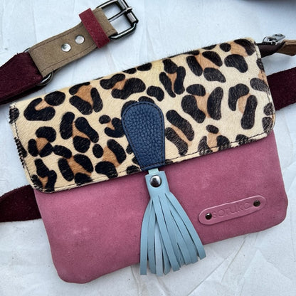 small square bag with dusty rose colored suede body, leopard print flap with light blue tassel, and maroon belt.