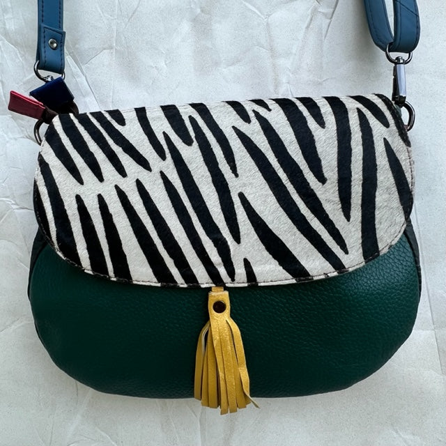 rounded forest  green purse with black and white animal print flap, yellow tassel, and blue strap.
