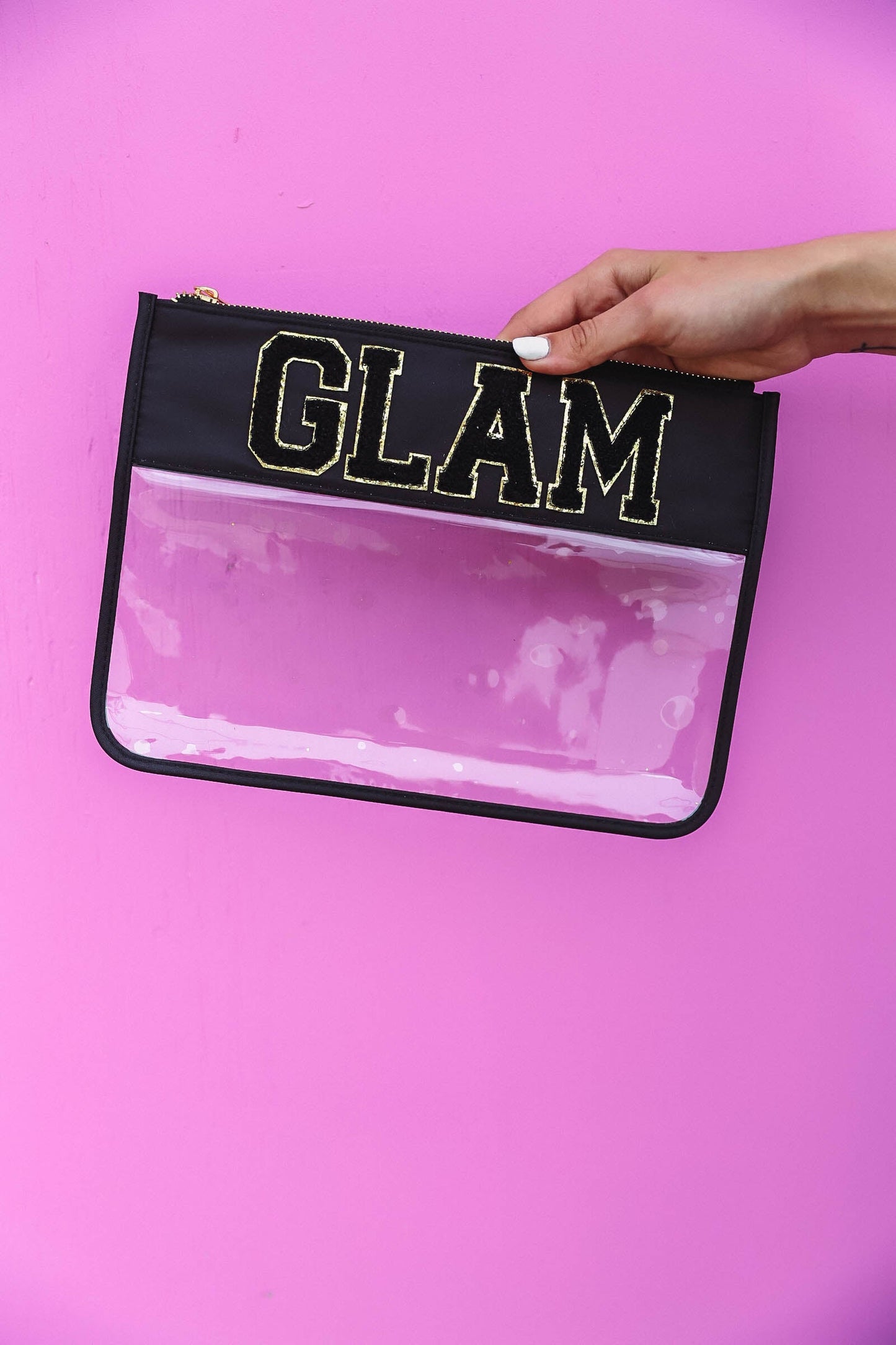 hand holding clear nylon bag with black trim and chenille patches that spell "glam".
