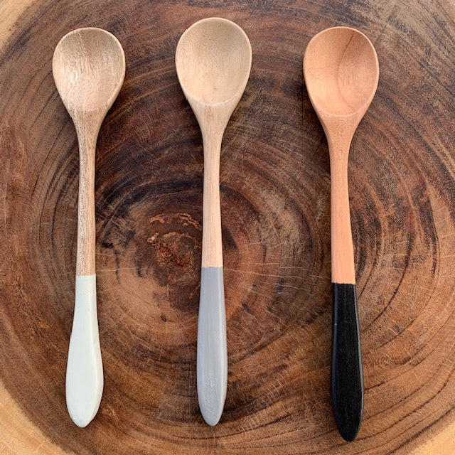 three hand carved mango wood spoons displayed on a round wood cookie slab