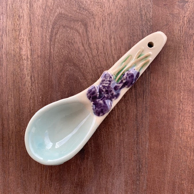 purple floral hand painted stoneware spoon on a dark wood background