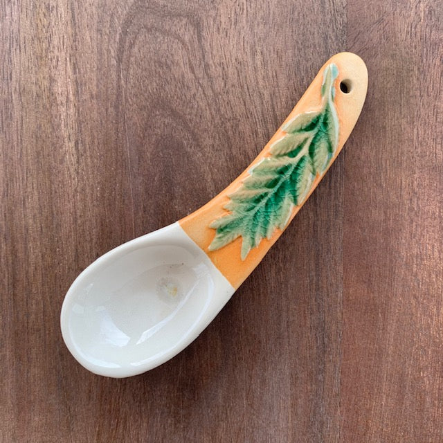 green leaf hand painted stoneware spoon on a dark wood background