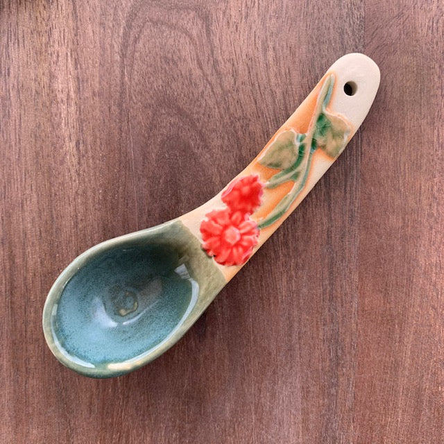 orange flower hand painted stoneware spoon on a dark wood background