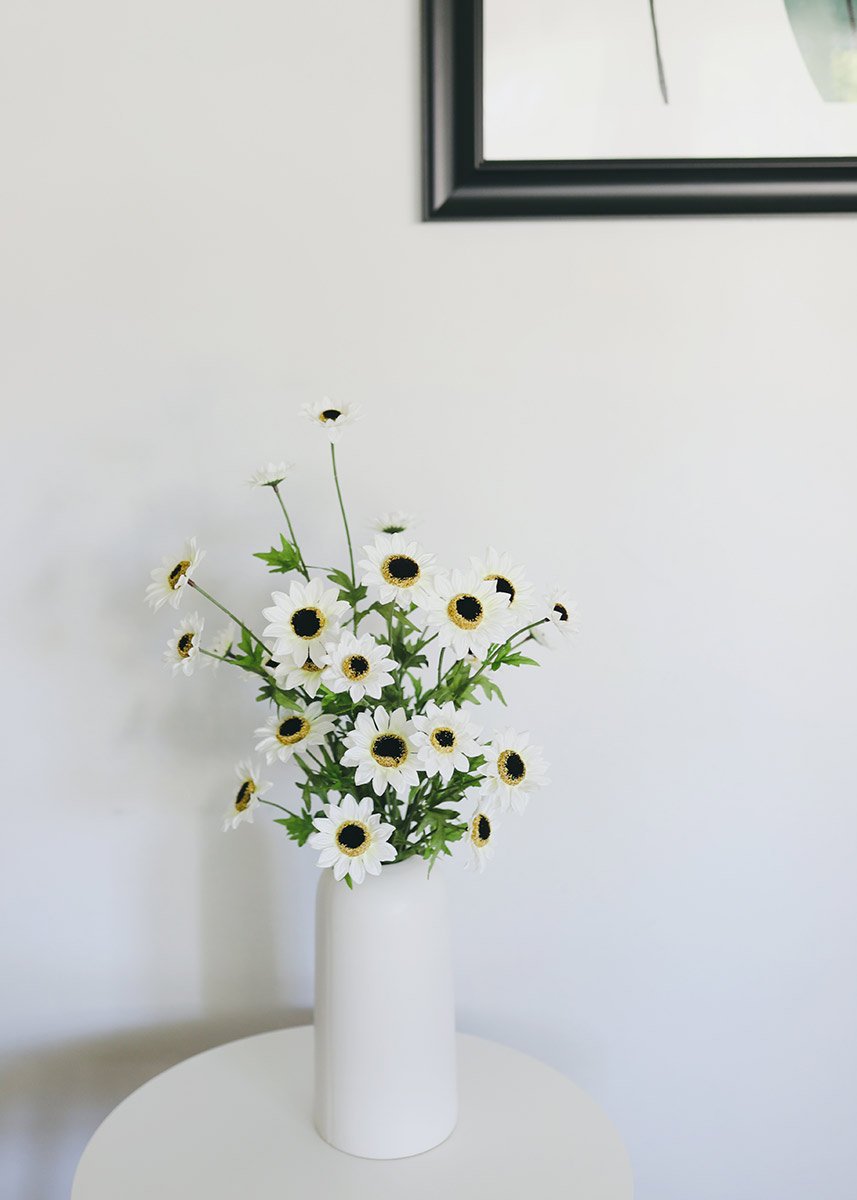 black-eyed susan bush displayed in a white vase under a mirror hanging on the wall