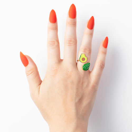 hand with orange painted fingernails wearing a avocado ring.