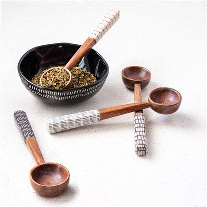 four different patterned wooden spoons displayed with a black bowl filled with spices on a white background