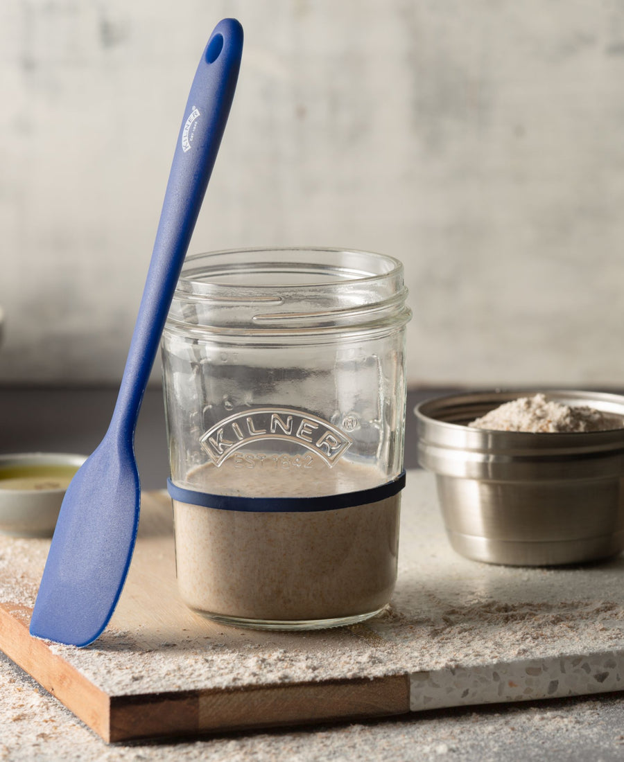 jar of sourdough starter on cutting board with spatula.