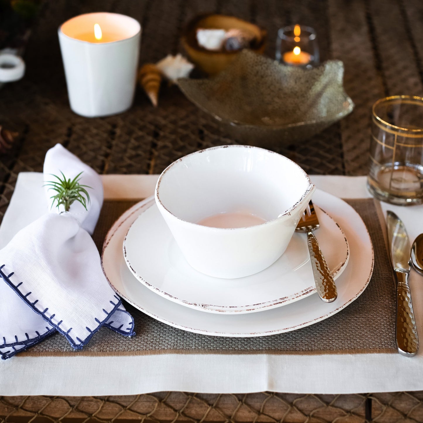table setting with plates, bowl and silverware with candles in the center.
