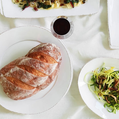 platters filled with bread and pastas and a glass of wine arranged on a white cloth.