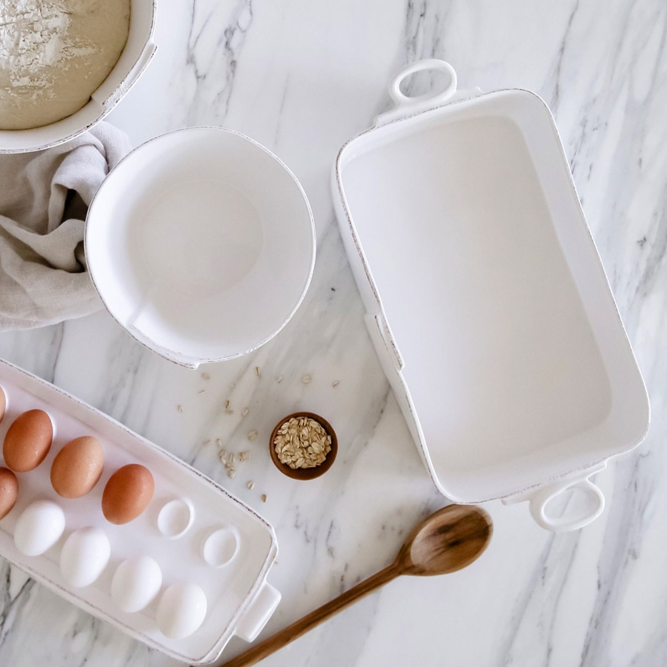 baking dish, bowl, and tray of eggs arranged on marble  countertop with spoon and seasonings.