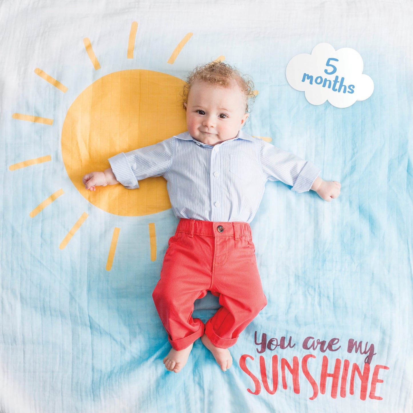 a baby boy laying on the you are my sunshine milestone blanket with the 5 month cloud tag next to him