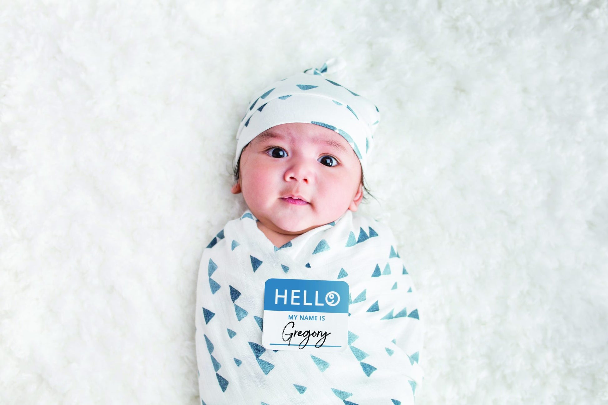 a baby wearing the hello world hat, wrapped in the swaddle with the name tag placed on the chest