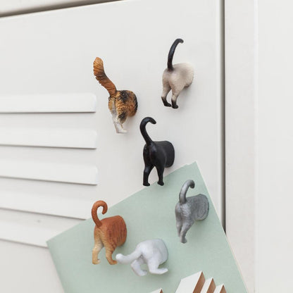 set of six cat butt magnets displayed on a white metal cabinet 