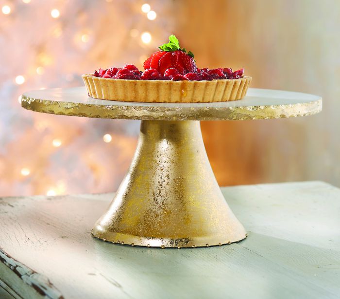 marble and golden cake stand displayed with a fruit tart on a white distressed table