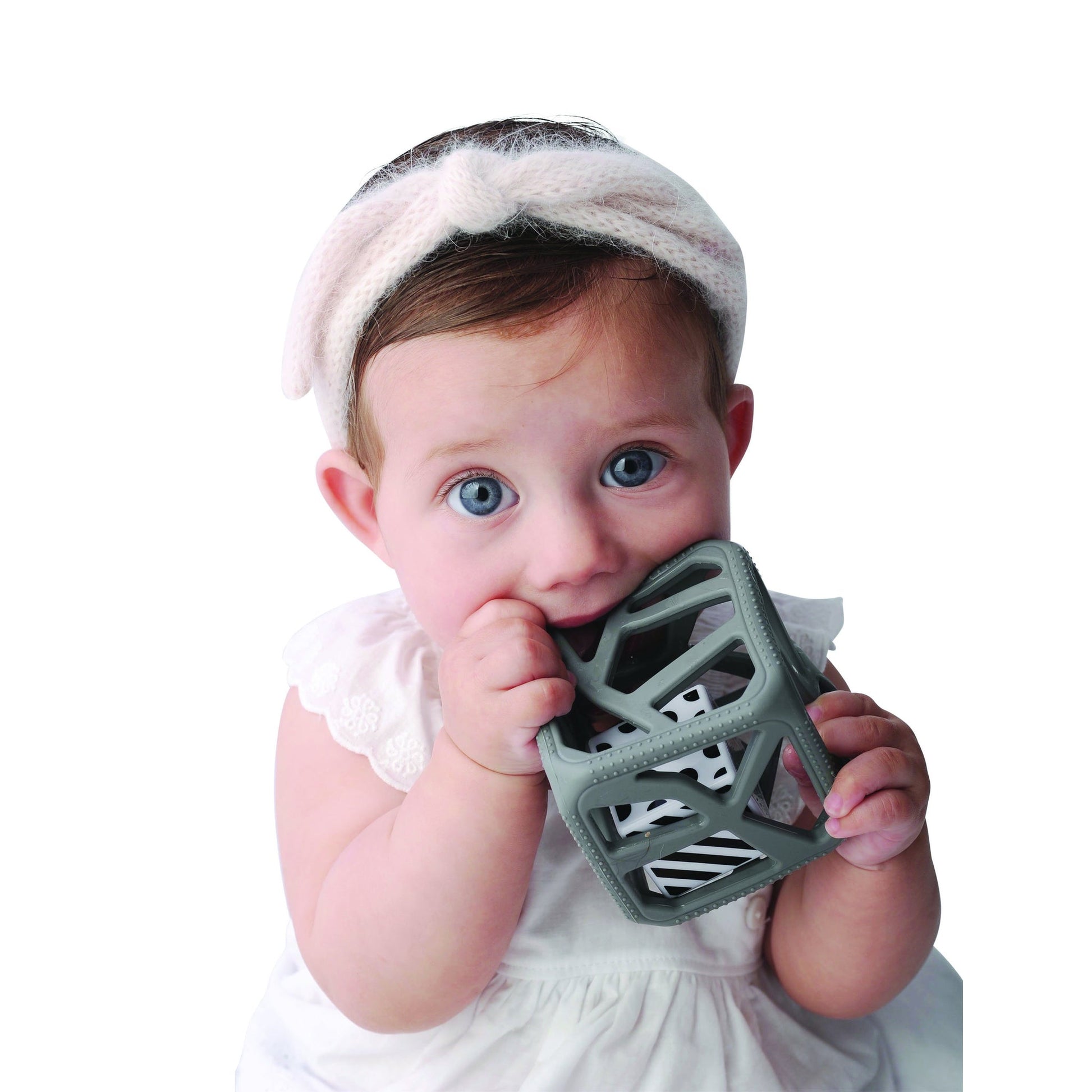a little girls chewing on the dark grey chew cube against a white background