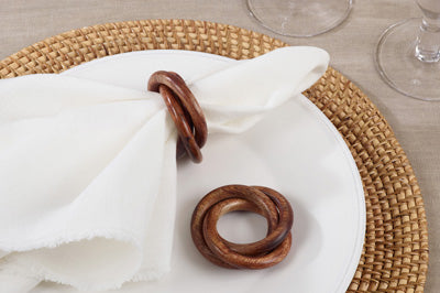 napkin ring on a white napkin and one not a napkin laying on a white plate on a table.