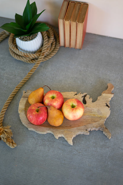 carved wood usa platter displayed with apples and pears on a light gray table with rope books a potted plant against a pale pink background