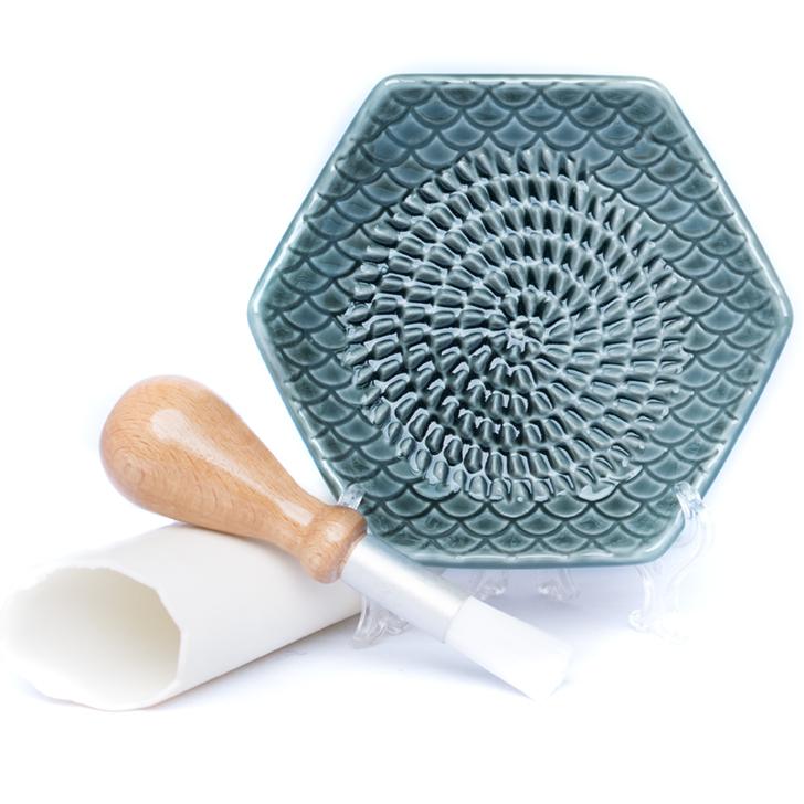 teal grate plate in easel with garlic peeler and cleaning brush nest to it on white background.