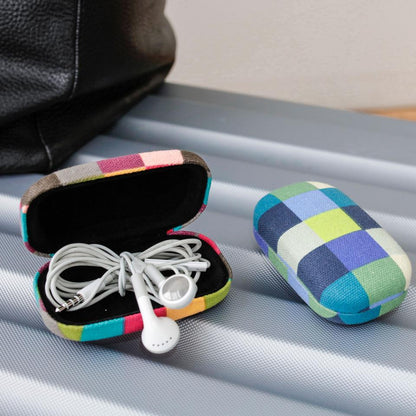 a plaid travel case open with earbuds inside and one closed displayed on a seat next to a black bag