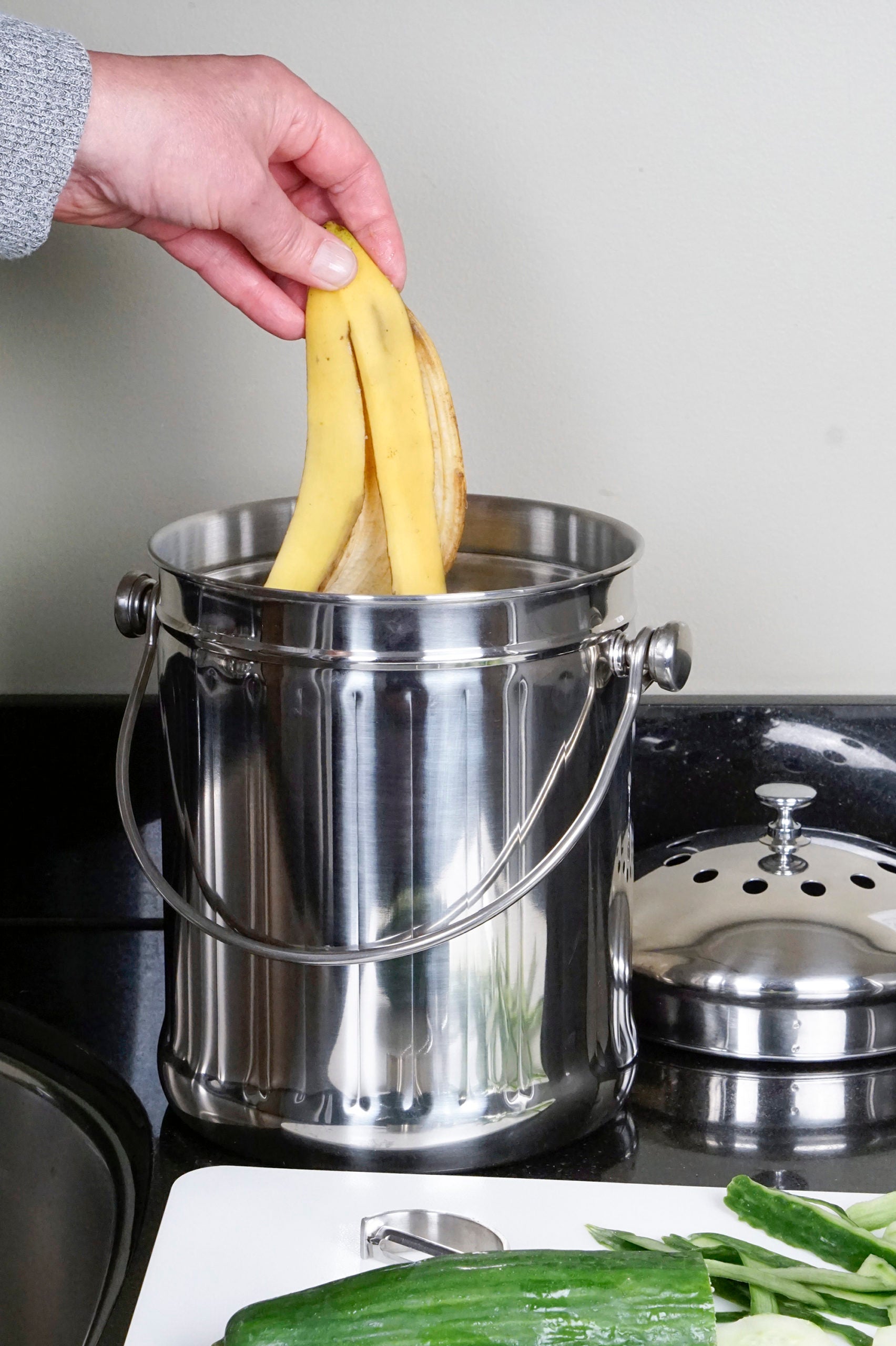 hand putting banana peel into compost pail on countertop.