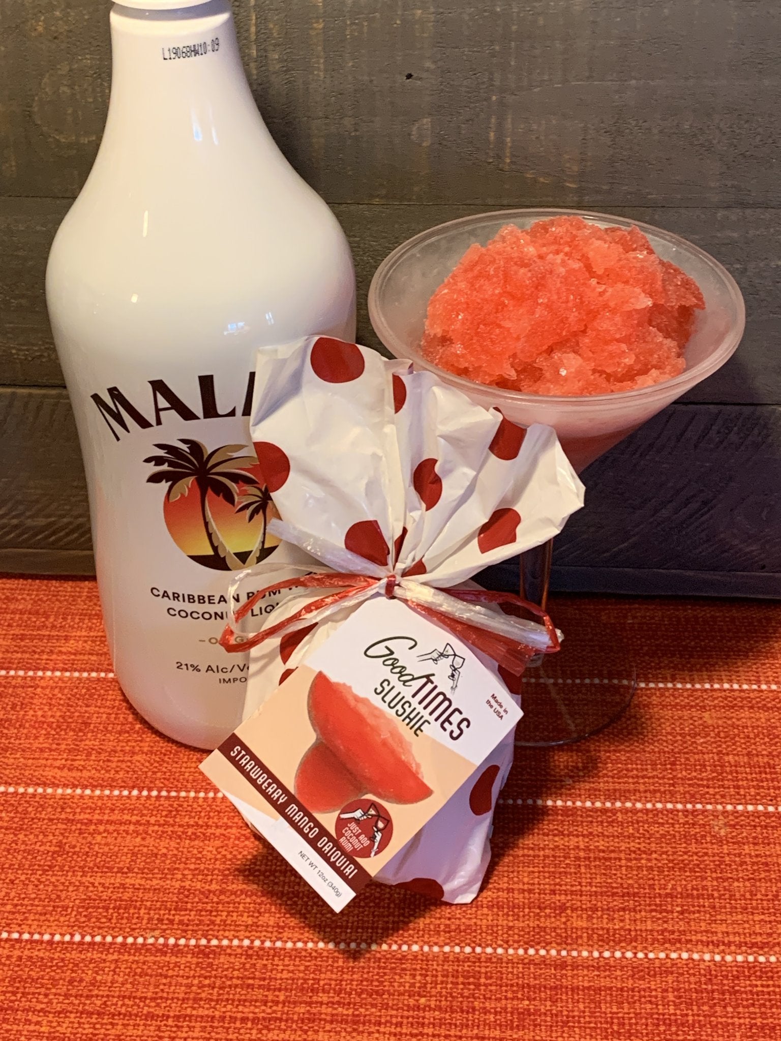 strawberry mango daiquiri slushie displayed in a glass next to the package and bottle of rum on a rust colored tablecloth