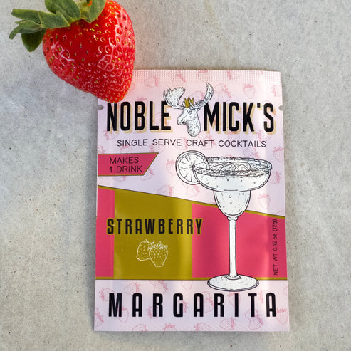 noble mick's single serve packet of Strawberry margarita mix on a bar top with a strawberry.