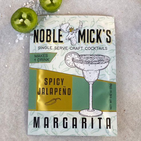 noble mick's single serve packet of spicy jalapeno margarita mix on a bar top with a salt and jalapeno slices.