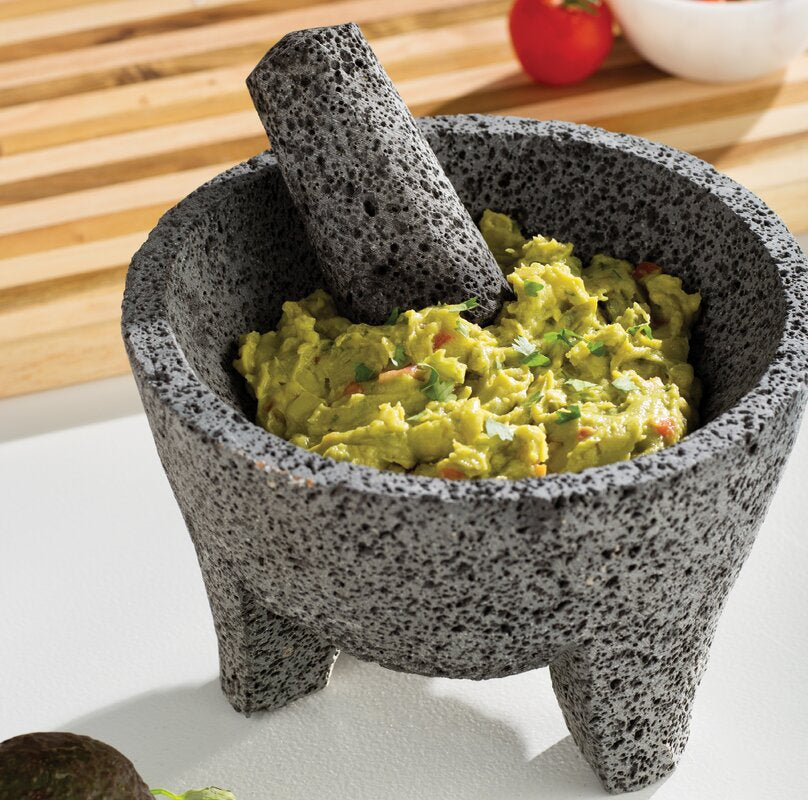 Molcajete and tejolote filled with guacamole on countertop.