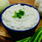 roasted garlic dip displayed in a blue bowl next to onions and garlic cloves on a wooden surface
