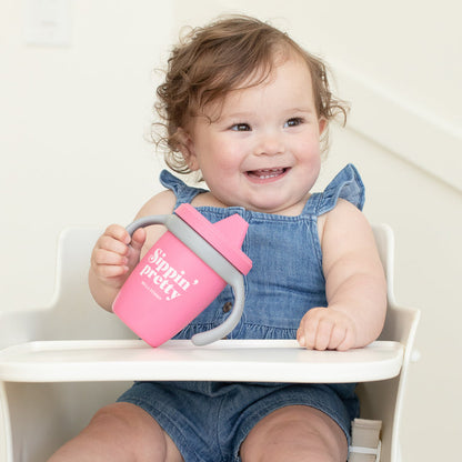a little girl sitting in a highchair and holding the sippin pretty happy sippy cup