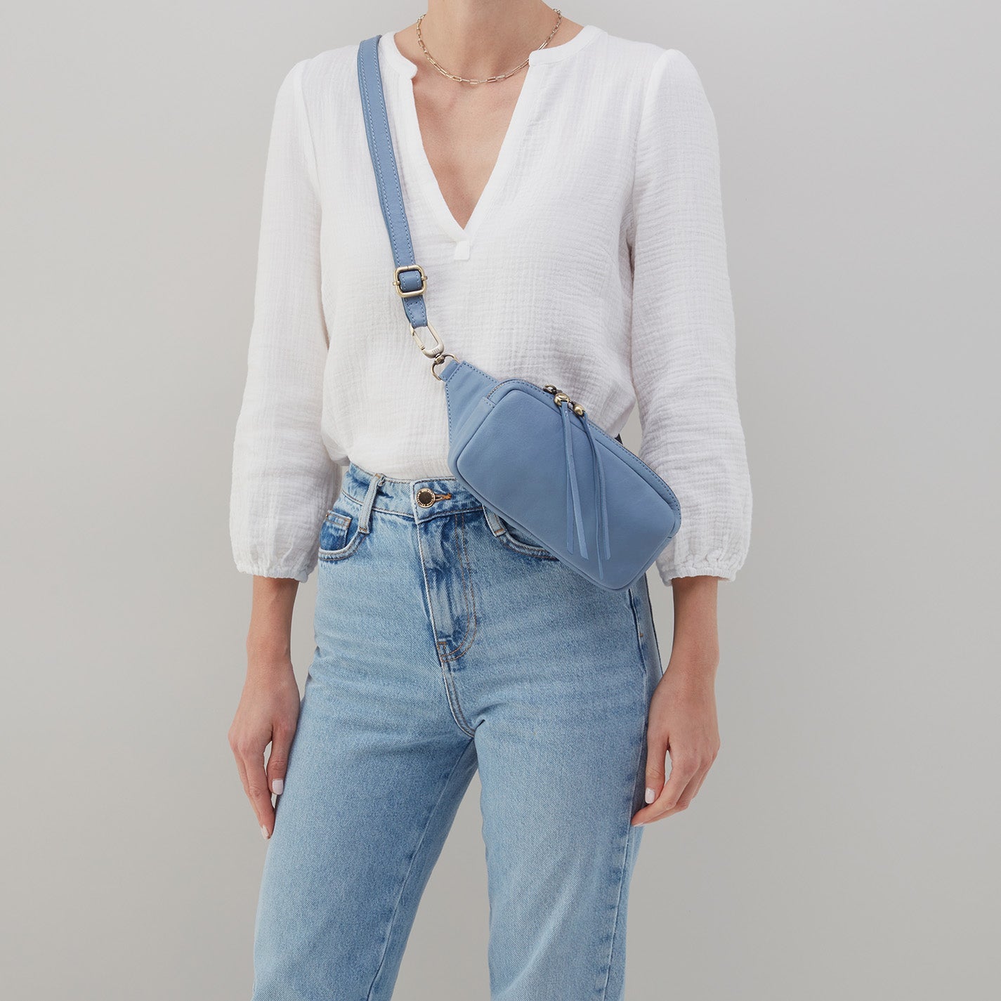 person wearing jeans and white blouse with provence blue shaker belt bag shaker belt bag over her shoulder.