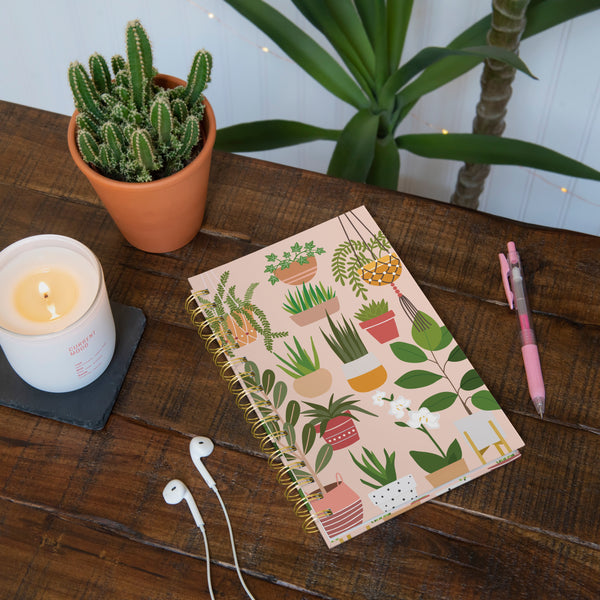 notebook on wooden table with earphones, pen, candle, and plants.