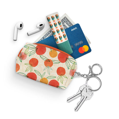 zipper pouch on white background with key on key ring and money, credit card, lip stick, and air pods coming out of it.