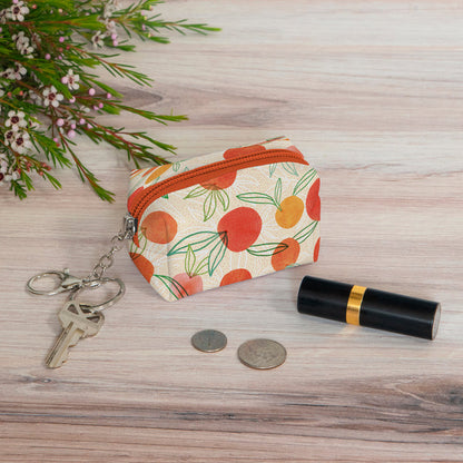 zipper pouch with key on ring sitting on wooden table with greenery, coins, and lipstick.