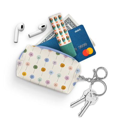 zipper pouch on white background with key on key ring and money, credit card, lip stick, and air pods coming out of it.