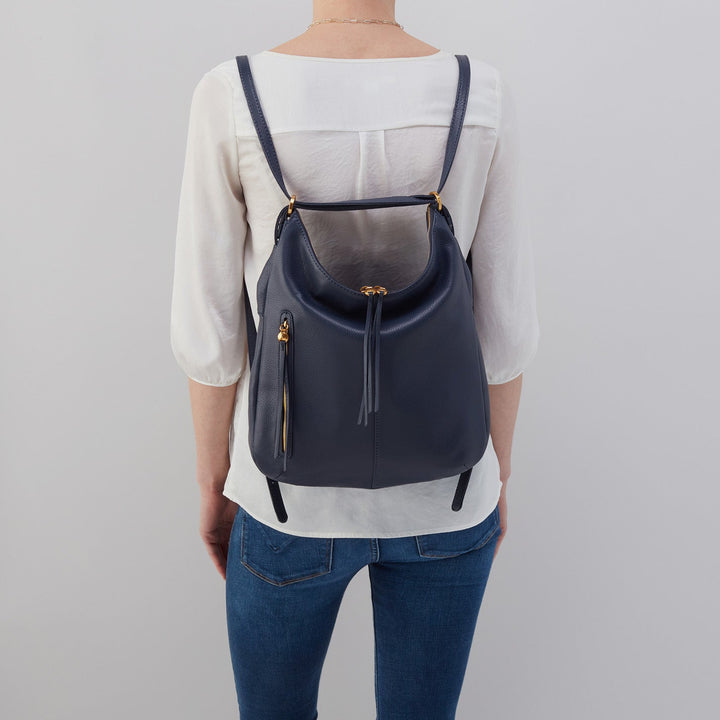 a woman wearing the sapphire merrin convertible backpack shoulder bag on her back against a light gray background