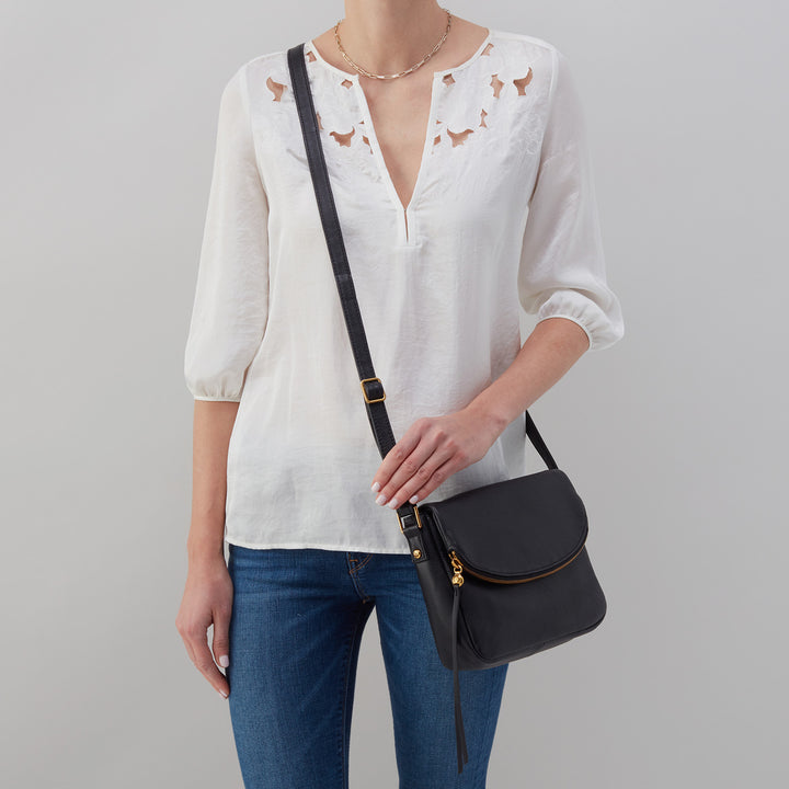 person wearing white shirt, blue jeans, and black fern bag.