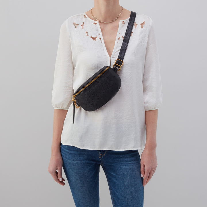 person wearing white shirt, blue jeans, and black fern bag as a crossbody.