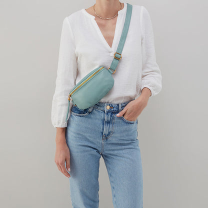 person wearing white shirt, blue jeans, and pale green fern bag as a crossbody.