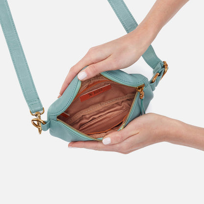 hands holding open pale green fern bag showing interior zip pockets and slip pockets.